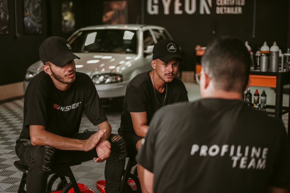 Team of men discussing in a garage with car detailing products and vehicle in the background.